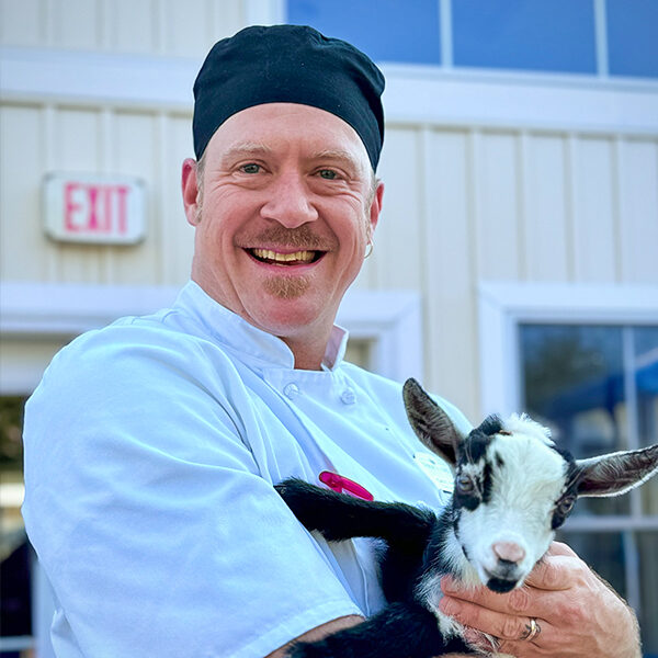 Chef Cary Allen smiling and holding a baby goat