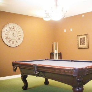 A billiard table with yellow walls and a clock and a photo on the wall